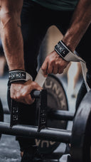 Atleta usando correas de halterofilia mientras sujeta una barra hexagonal con pesas, preparándose para realizar un levantamiento