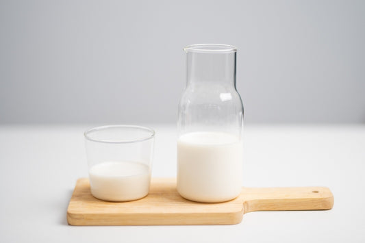 Un vaso de cristal con leche junto a una botella de cristal con leche